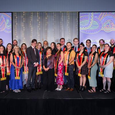 2023 Aboriginal and Torres Strait Islander Sashing Ceremony students pose on stage with Professor Kris Ryan, Deputy Vice-Chancellor (Academic), and Professor Bronwyn Fredericks, Deputy Vice-Chancellor (Indigenous Engagement).