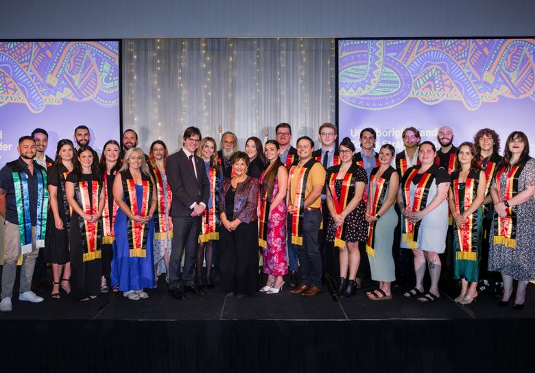 2023 Aboriginal and Torres Strait Islander Sashing Ceremony students pose on stage with Professor Kris Ryan, Deputy Vice-Chancellor (Academic), and Professor Bronwyn Fredericks, Deputy Vice-Chancellor (Indigenous Engagement).