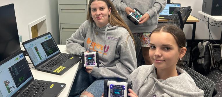 Students wearing InspireU jumpers pose at computers