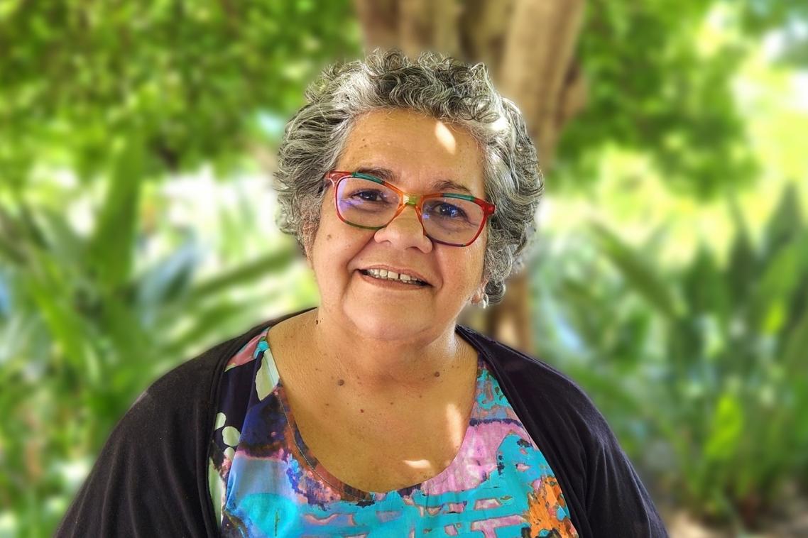 Smiling woman sitting under trees and surrounded by greenery in UQ gardens