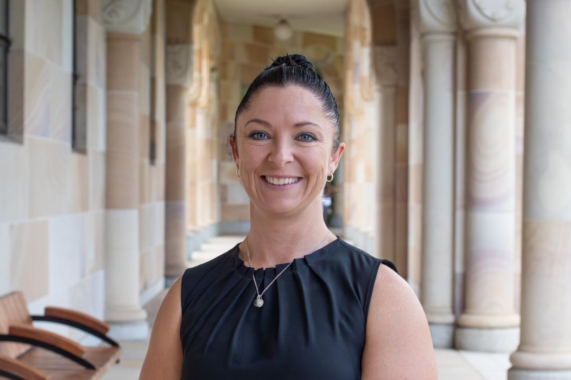 Smiling woman standing under sandstone pillars in UQ Great Court